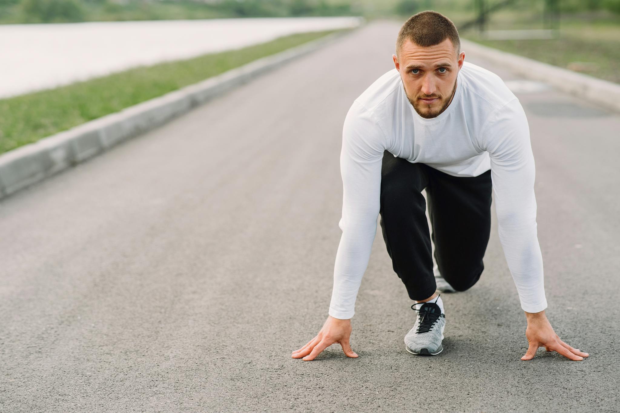 A man in sportswear prepares to run on an empty road, embodying fitness and determination.